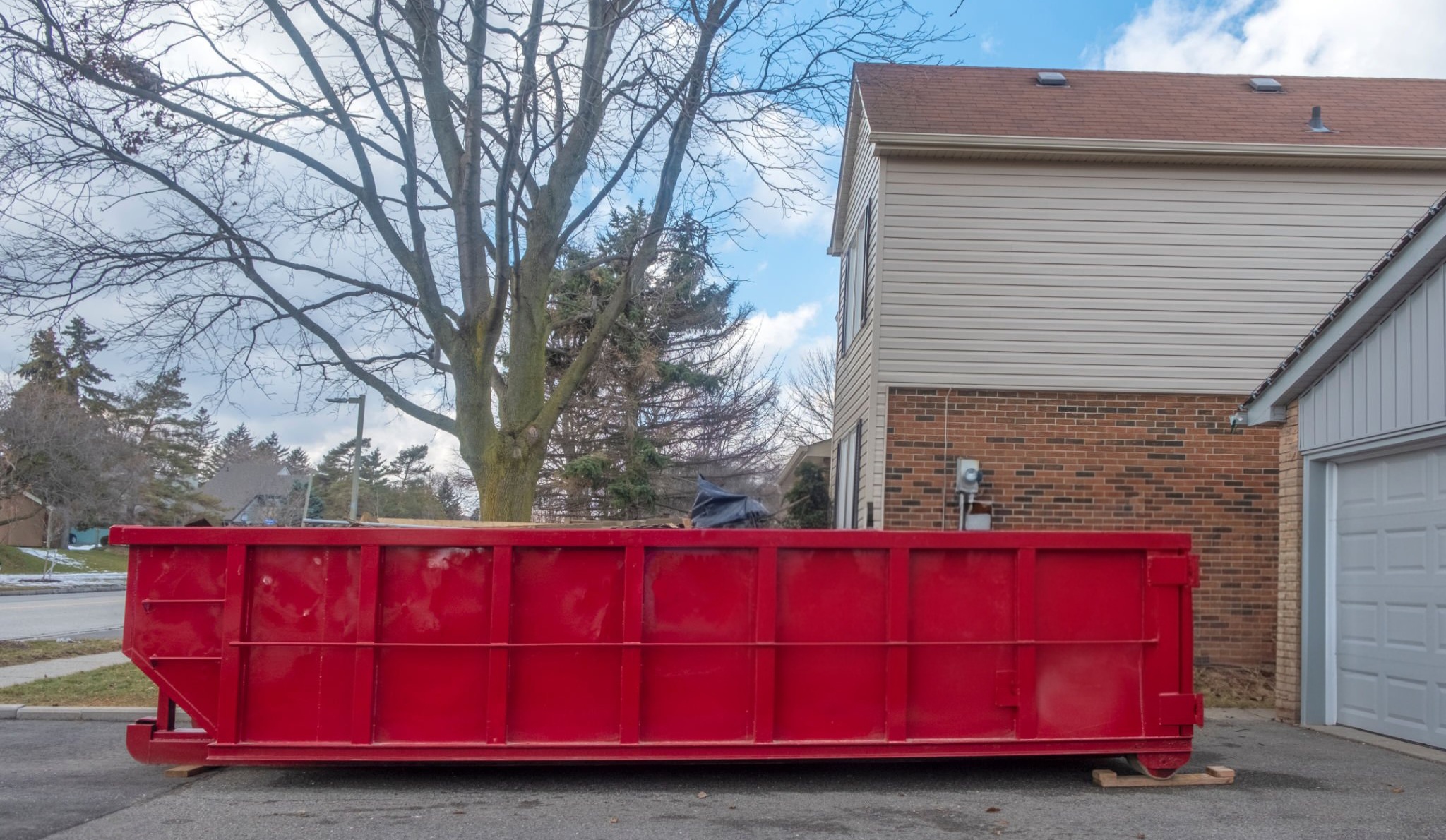 red dumpster bin on the driveway of a suburban house